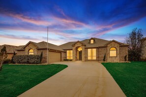 A two-story house with a stone facade, a front garage, and a well-maintained lawn. - 5-Bed/2-Bath Pool & Backyard Retreat (Waxahachie)