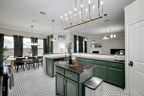A kitchen with green cabinets, a granite countertop, a dining area with a table and chairs, and pendant lighting.