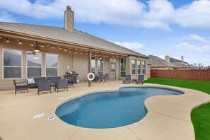 A backyard with a swimming pool, patio furniture, and a barbecue area.