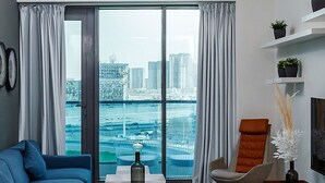 Een moderne woonkamer met uitzicht op de stad, een blauwe bank, een bruine fauteuil en een ronde tafel met een fles.