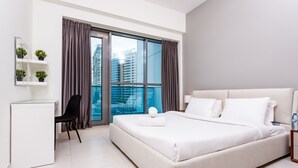 Een moderne hotelkamer met een groot bed, een bureau, een stoel en een stadszicht door grote ramen.