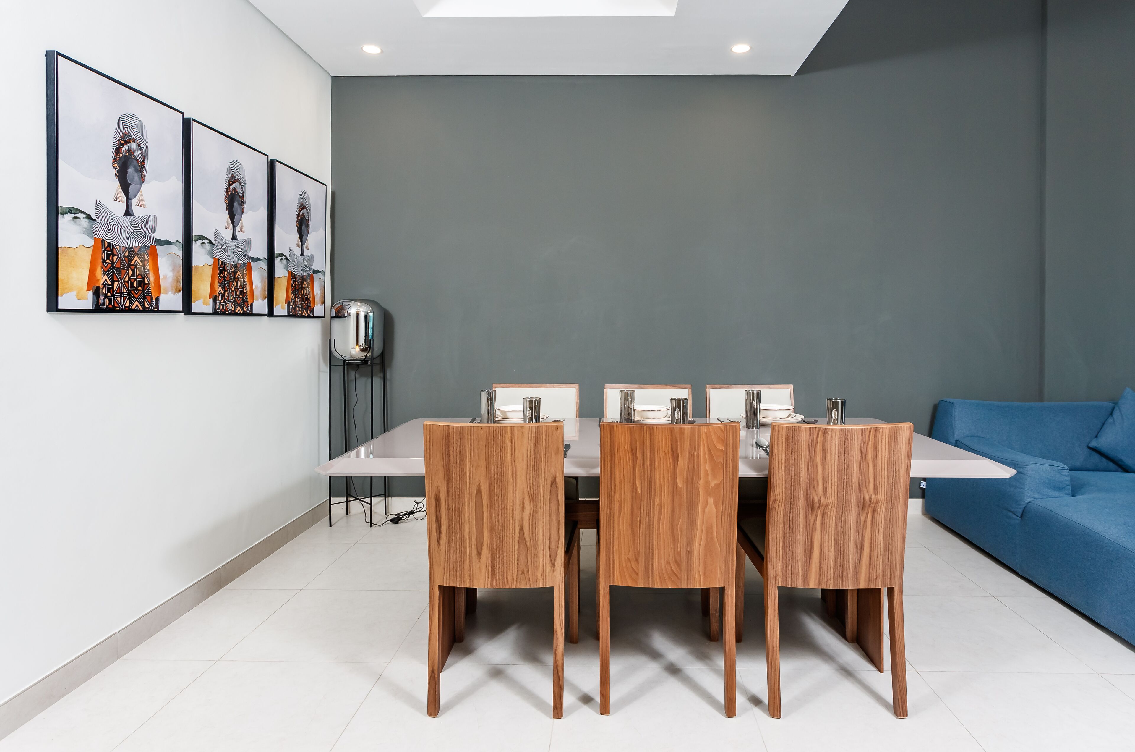 A modern dining area with a rectangular table, four wooden chairs, and a blue sofa.