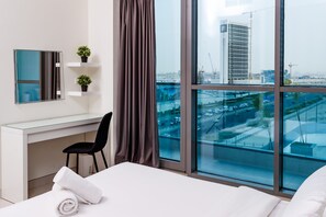 A modern hotel room with a large window, a desk, a chair, and a bed. - Spacious 2BR apartment with rooftop pool The Bay DT by 360 Vacation (Dubai)