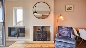 A cozy living room with a fireplace, a round mirror, and a comfortable blue armchair. - Host & Stay | Watch House (Scarborough)
