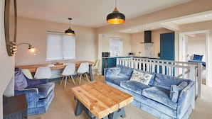 A cozy living area with a wooden coffee table, blue sofas, and a kitchen in the background. - Host & Stay | Watch House (Scarborough)