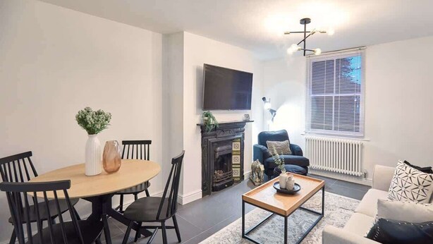 A modern living room with a fireplace, a television mounted on the wall, a dining table with chairs, and a sofa. - Host & Stay | High Street Cottage (Norton)