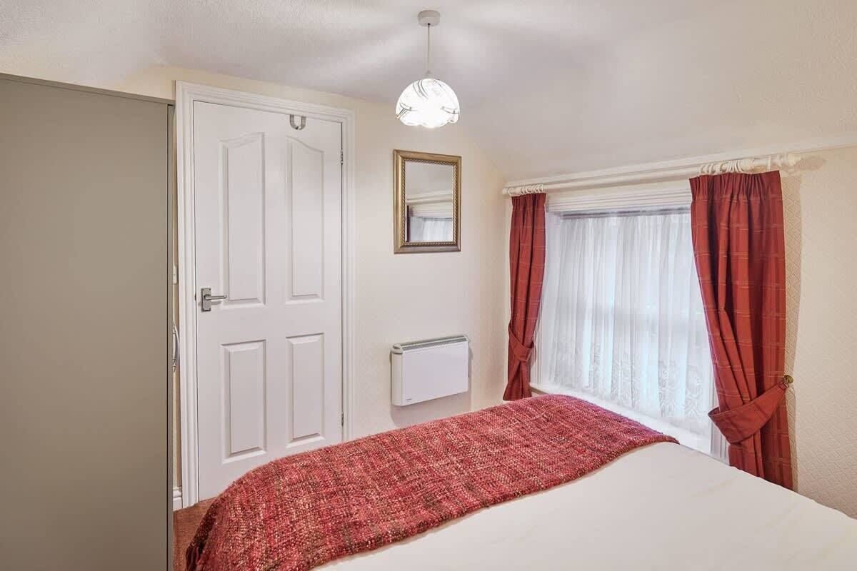 Een slaapkamer met een bed, een witte deur, een spiegel, een radiator en een raam met gordijnen.