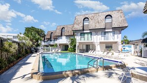 Un área de piscina con sillones de descanso y un edificio con balcones.