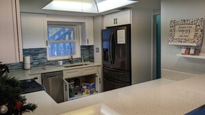 Una cocina moderna con armarios blancos, un refrigerador de acero inoxidable, lavavajillas y una ventana con vidrio tintado de azul.