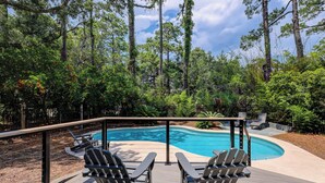 Un área de piscina con dos sillas Adirondack, rodeada por una terraza de madera y una barandilla de metal.