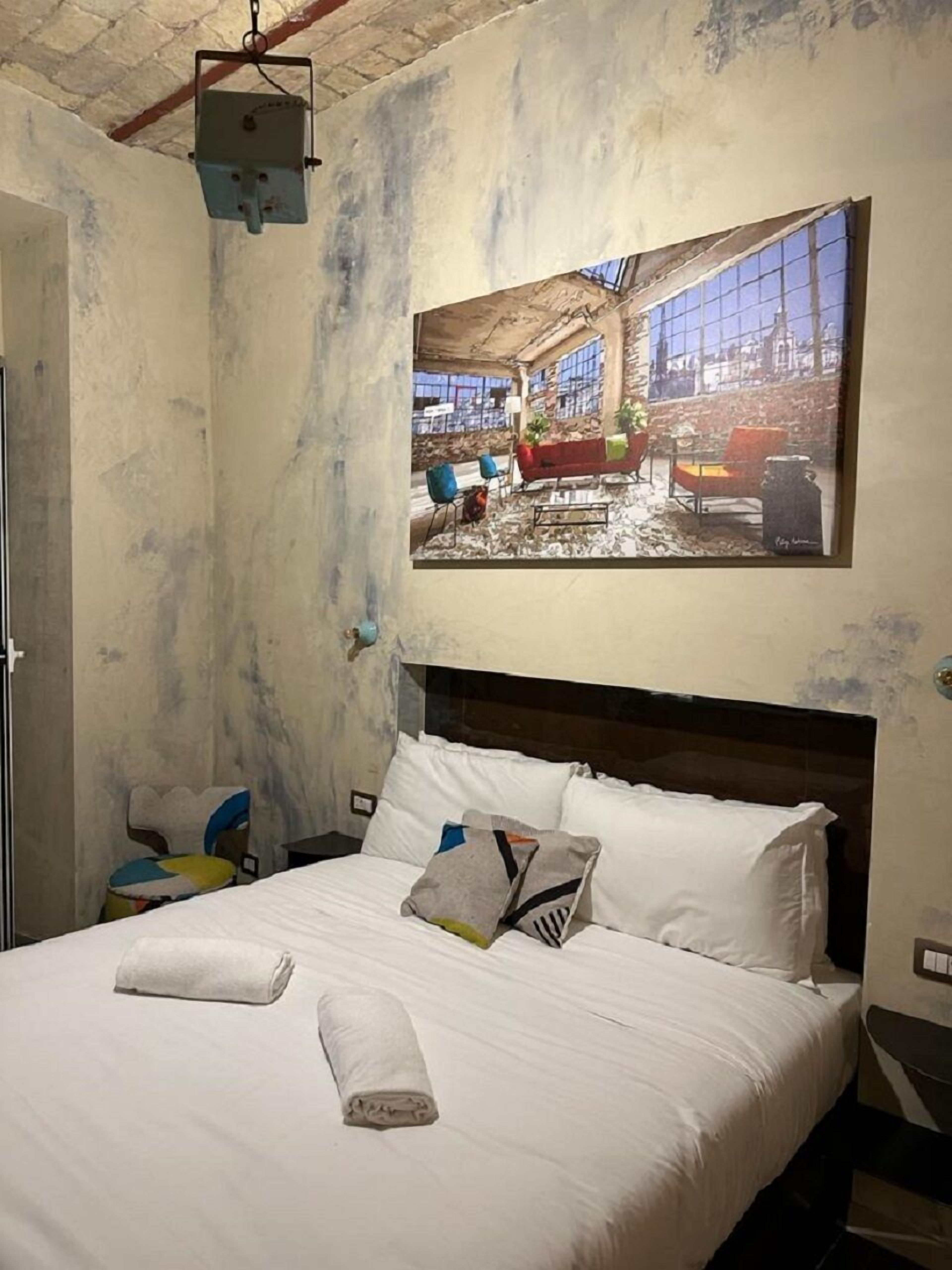 Ein Hotelzimmer mit einem Bett, einem Kopfteil, einem Wandbild und einer Deckenleuchte.