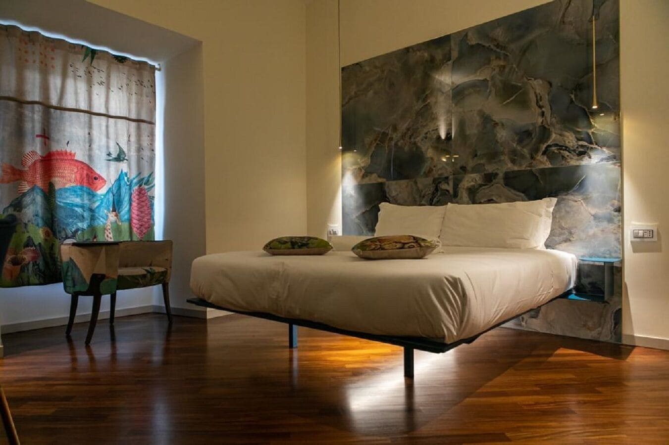 Un dormitorio con cama, una silla, un cuadro abstracto grande en la pared y una ventana con cortinas.