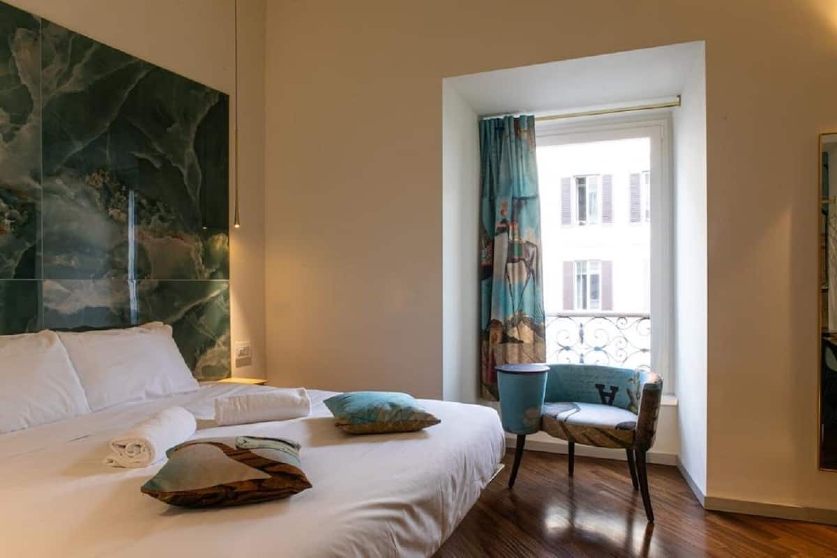 Habitación de hotel con una cama grande, una silla, una ventana con cortinas y una pared con un cuadro abstracto de gran tamaño.