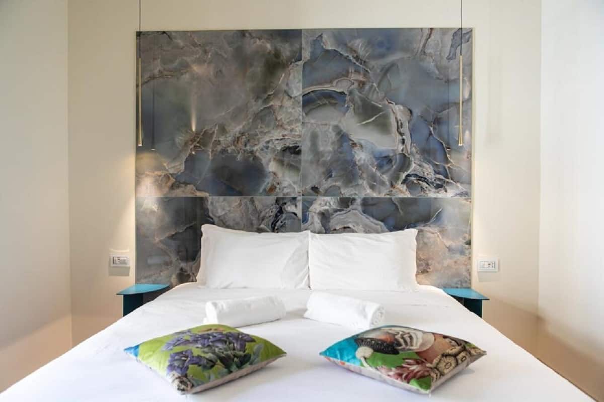 Habitación de hotel con un cuadro abstracto grande en la pared, una cama con ropa de cama blanca y dos almohadas coloridas.