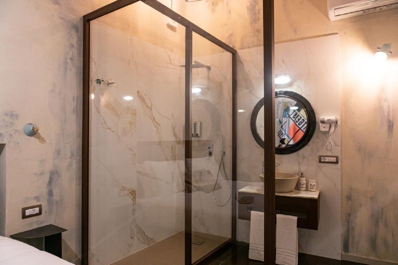Ein modernes Badezimmer mit einer Glaskabine zur Dusche, einem runden Spiegel und einer Wand mit Marmorfliesen.