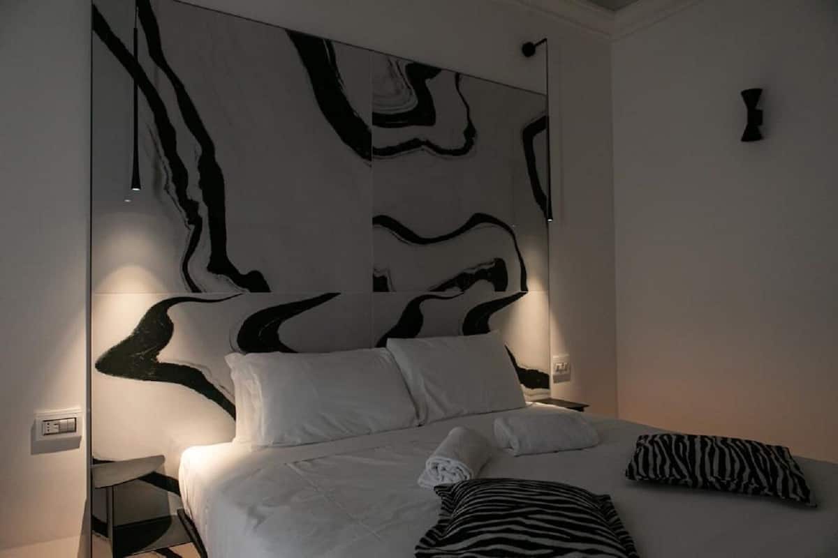 Un dormitorio moderno con un cuadro abstracto grande en la pared, una cama con ropa de cama blanca y una almohada con estampado de cebra.