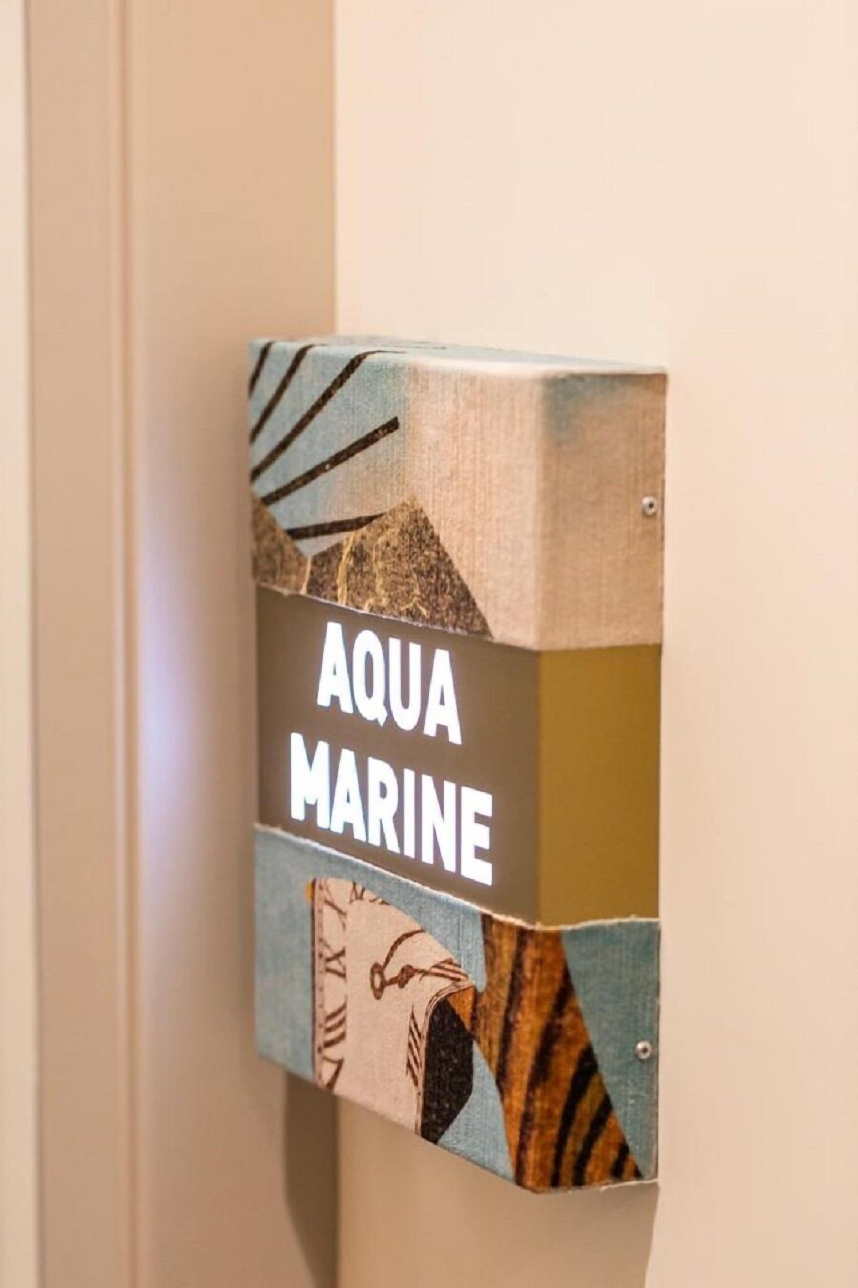 A sign with the words "AQUA MARINE" on a textured wall.