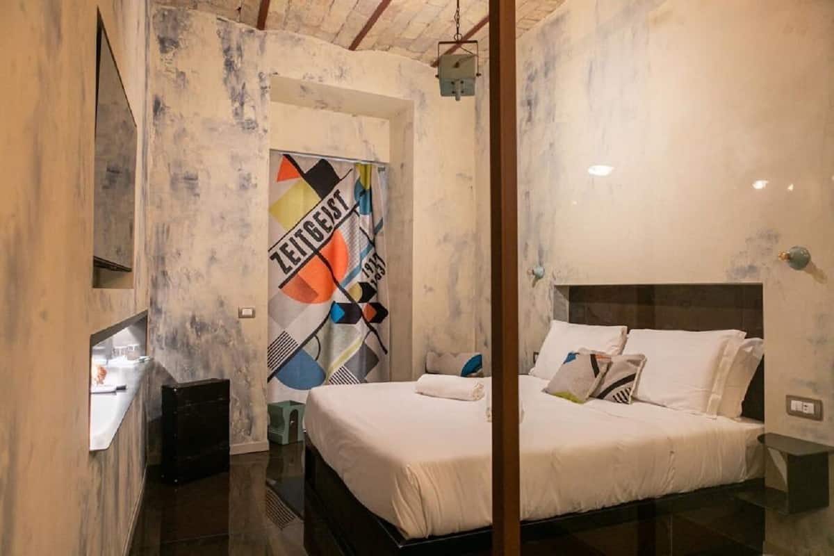 Un dormitorio con una cama, una mesita de noche, un espejo y una pared decorada con un diseño abstracto y colorido.