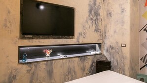 A room with a TV mounted on the wall, a shelf with a vase and glasses, and a bed with a white cover. - Bhr Cavour 150 (Rome)