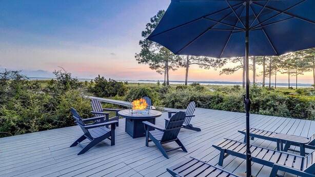 A deck with outdoor seating, a fire feature, and a view of the ocean at sunset.