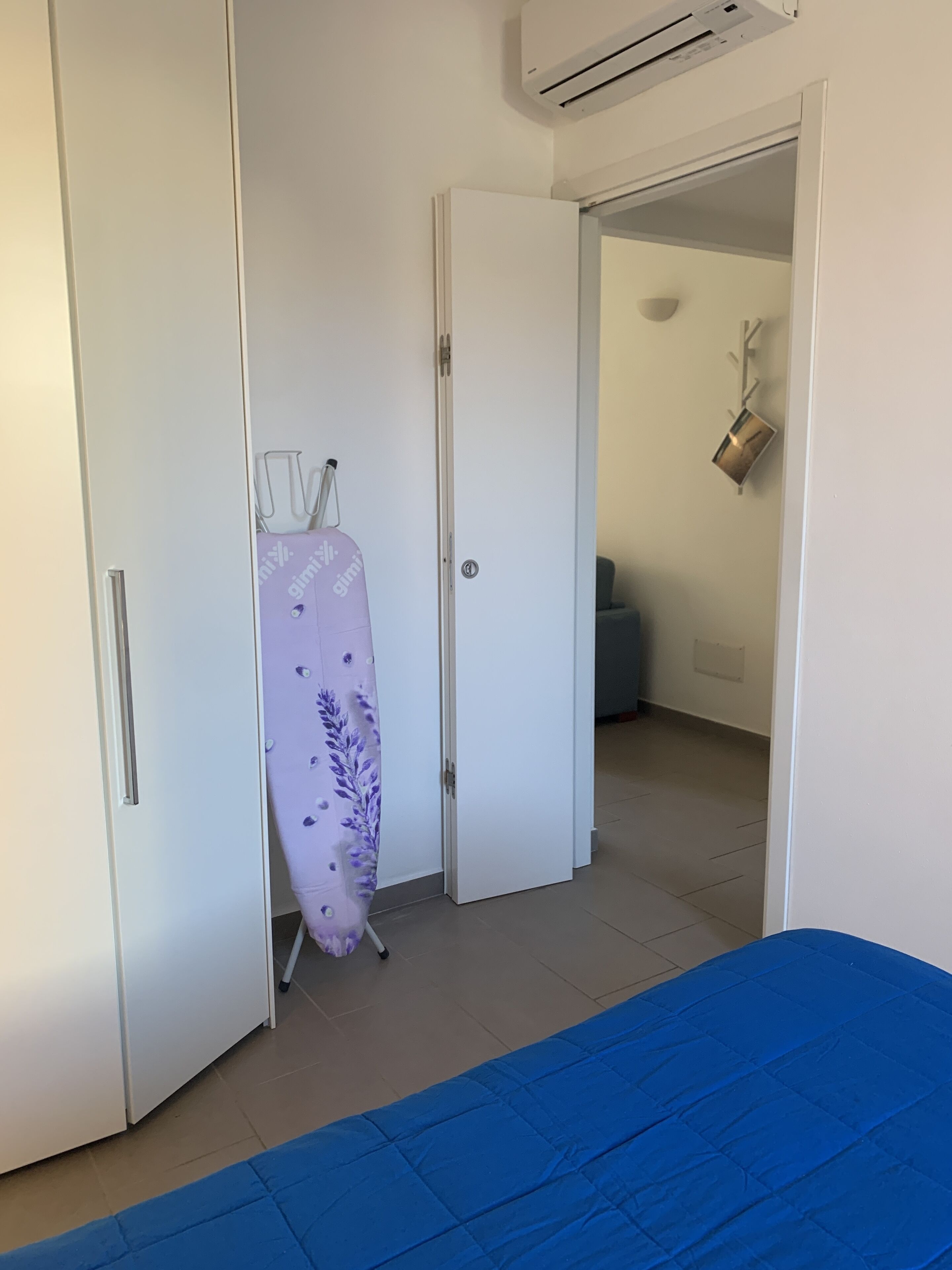 A bedroom with a bed, a wardrobe, and an ironing board.