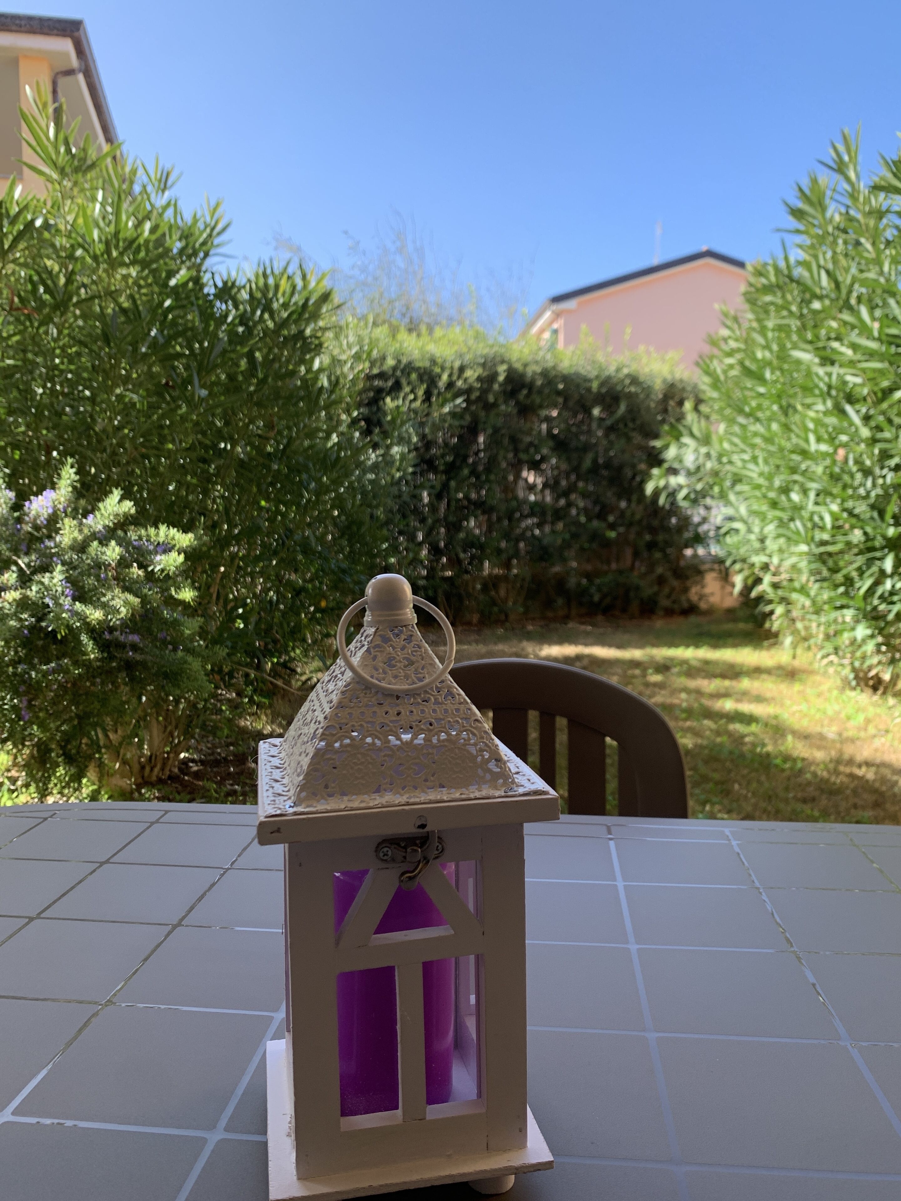 Une petite lanterne blanche, dont l’intérieur est violet, posée sur une terrasse carrelée.