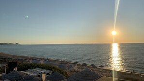 Blick auf einen Strand bei Sonnenuntergang über dem Wasser, ein klarer Himmel und einige Gebäude mit Strohdächern.
