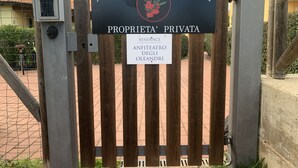 Ein hölzernes Tor mit einem Schild, das 'ANFITEATRO DEGLI OLEANDRI' und 'PRIVATES WOHNANLAGE' anzeigt.