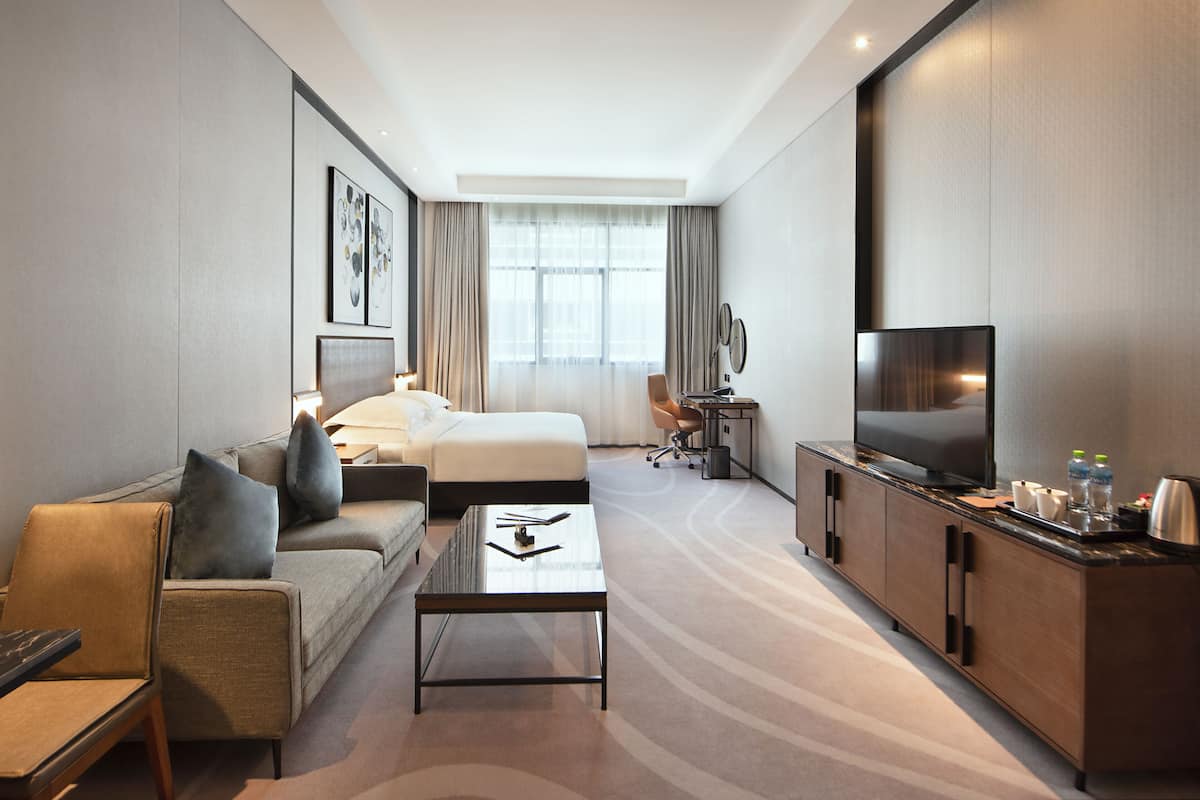 Une chambre d’hôtel comprenant un lit, un canapé, une table basse, une télévision et un bureau avec une chaise.