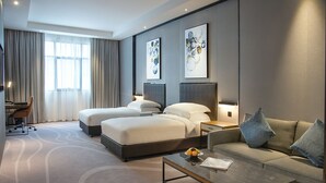 Et moderne hotelværelse med to senge, en sofa, et sofabord og kunst på væggene.