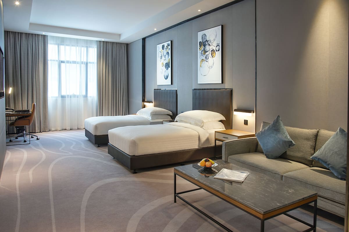 Une chambre d’hôtel moderne équipée de deux lits, d’un canapé, d’une table basse et ornée d’œuvres d’art sur les murs.