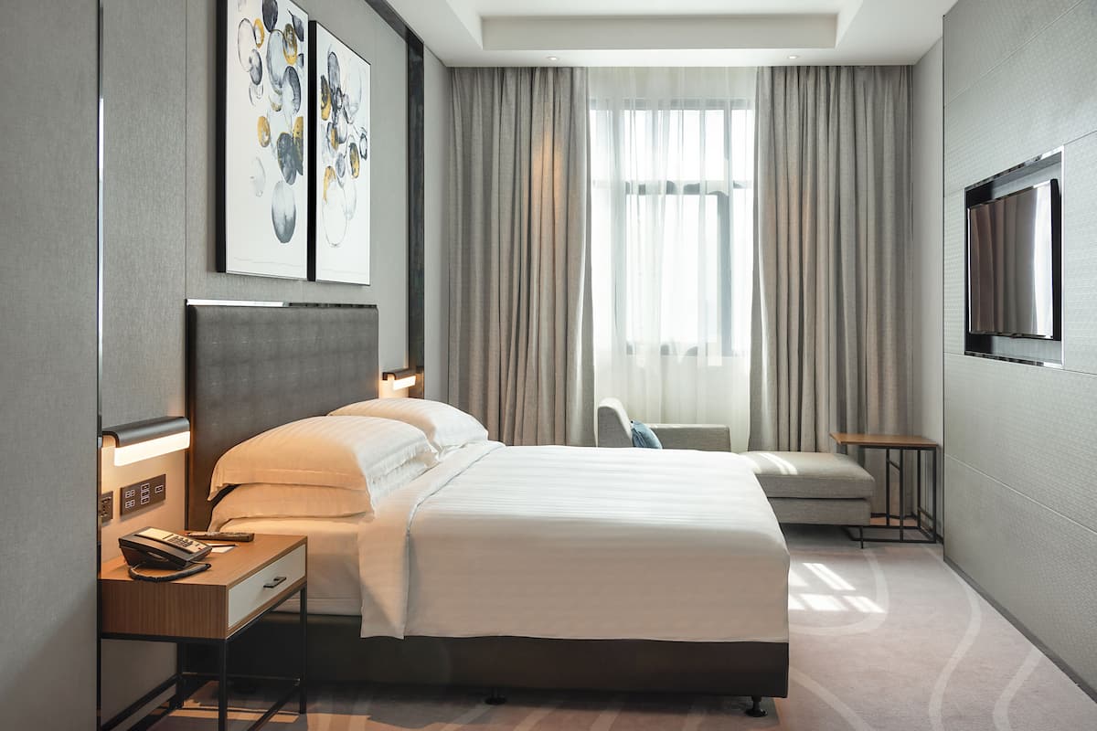 Une chambre d’hôtel moderne avec un grand lit, une table de chevet avec une lampe, un petit bureau et un téléviseur fixé au mur.