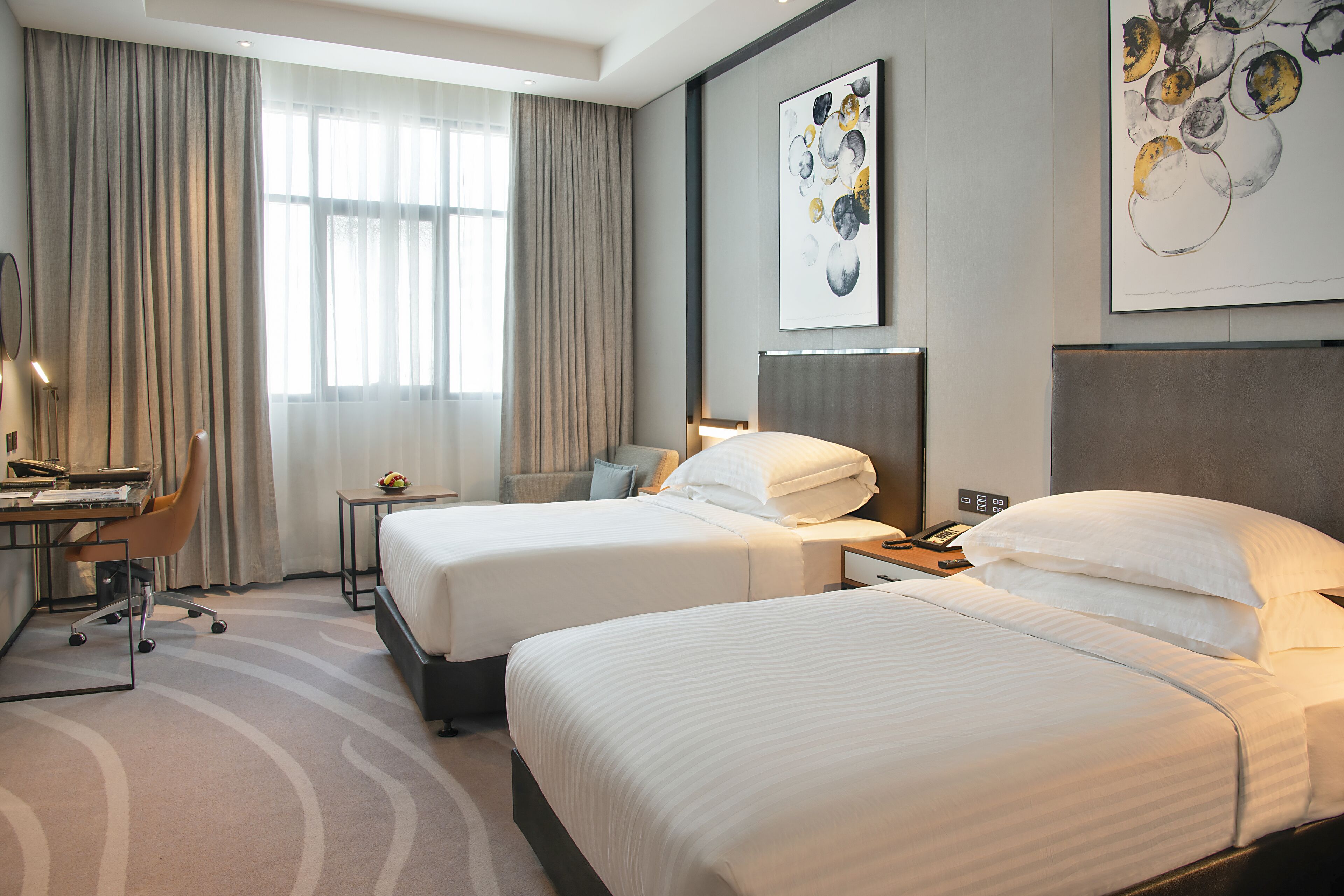 Een hotelkamer met twee bedden, een bureau, een stoel en kunstwerken aan de muur.