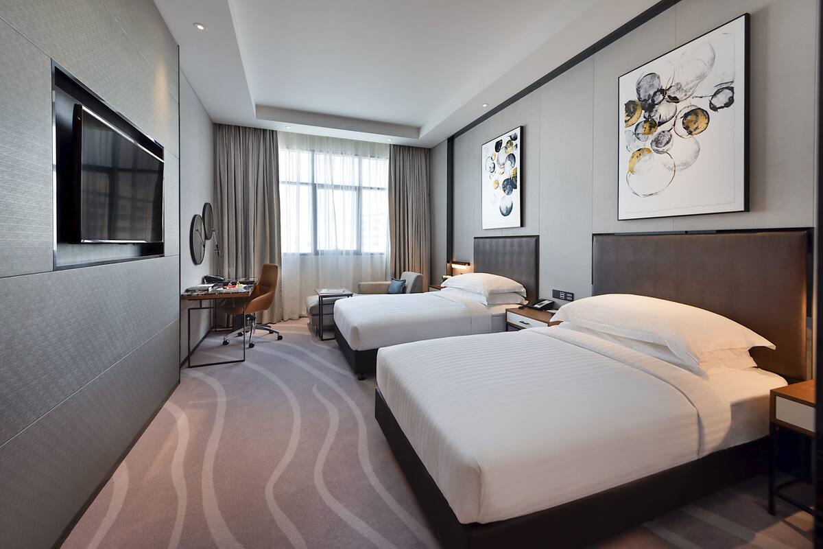 Une chambre d’hôtel avec deux lits, un bureau avec une chaise, une télévision et des œuvres d’art accrochées aux murs.