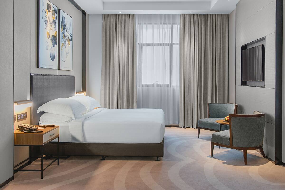 Une chambre d’hôtel équipée d’un lit, d’un bureau avec un téléphone, d’une chaise et d’un téléviseur fixé au mur.