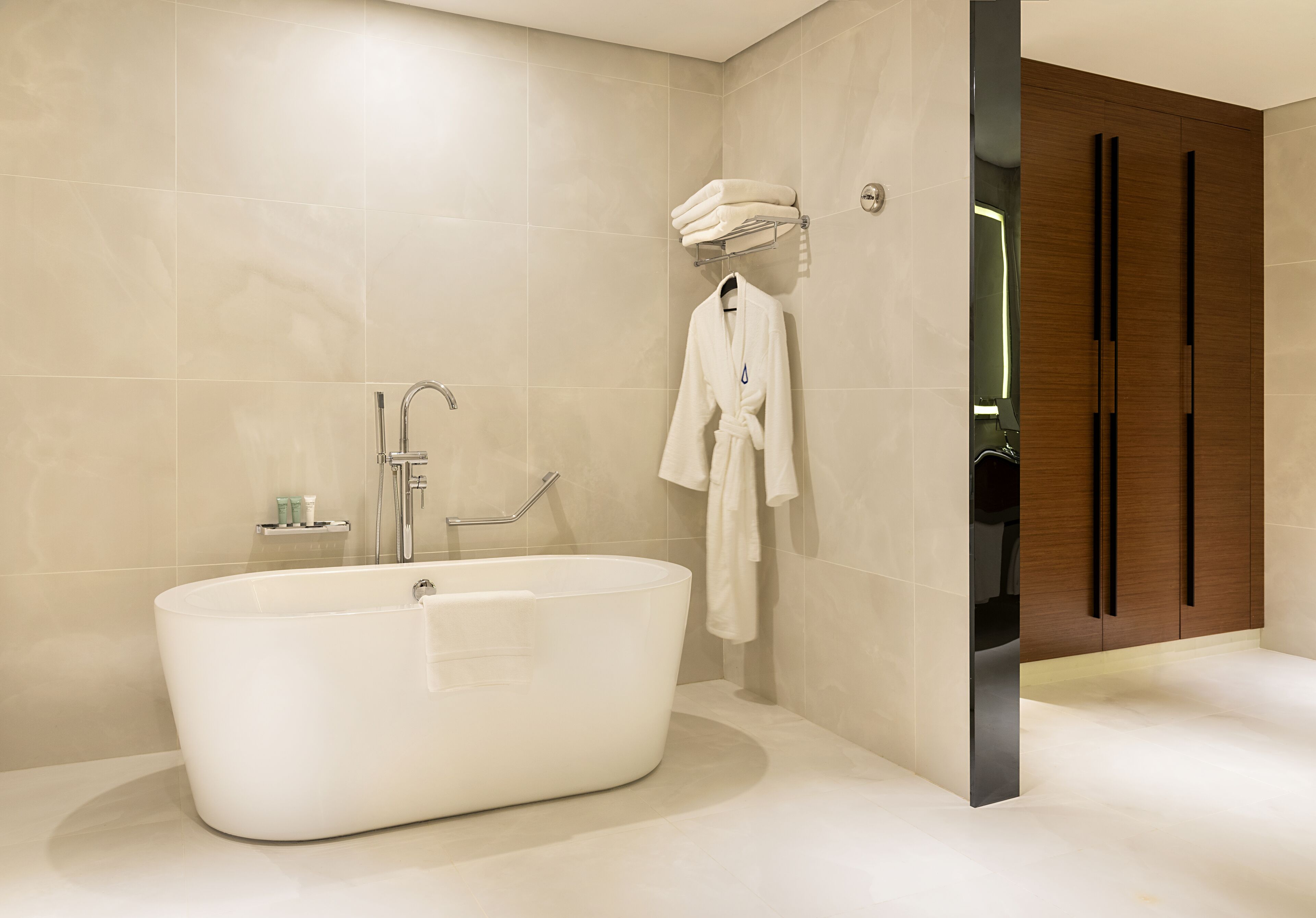 A modern bathroom with a freestanding bathtub, a towel rack with towels, and a wooden wardrobe.