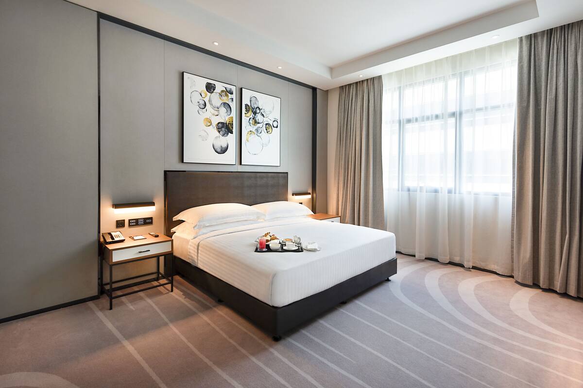 Une chambre d’hôtel moderne avec un grand lit, une table de chevet dotée d’un téléphone et d’une lampe, et deux tableaux abstraits accrochés au mur.