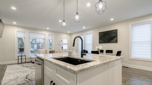 A modern kitchen with a large island, white cabinetry, and pendant lighting. - 65 on the Main in the heart of Kingsville (Kingsville)