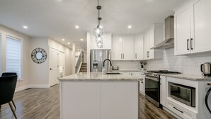 A modern kitchen with white cabinetry, a central island, stainless steel appliances, and a chandelier. - 65 on the Main in the heart of Kingsville (Kingsville)