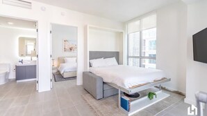 Une chambre moderne avec un lit, une table de chevet et une vue sur la ville grâce à de grandes fenêtres.