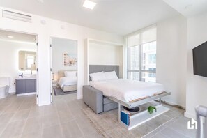 A modern bedroom with a bed, bedside table, and a view of the city through large windows.