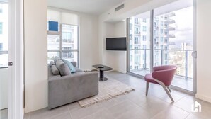 Un salon moderne avec un canapé gris, une petite table, un fauteuil rouge et un téléviseur fixé au mur.
