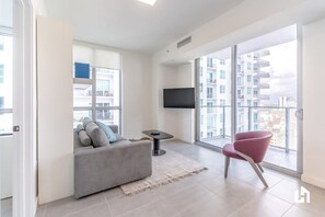 A modern living room with a grey sofa, a small table, a red chair, and a TV mounted on the wall.