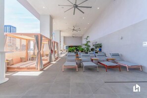 Un salon intérieur moderne doté de ventilateurs de plafond, d’un espace détente avec des fauteuils et offrant une vue sur le paysage urbain.
