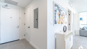 A modern hallway with white walls, a white door, and a white console table with a decorative item. - Downtown Stay | Restaurant, Gym, Pool & CoWork! (Miami)