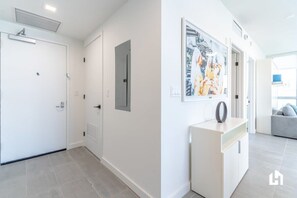 Un couloir moderne aux murs blancs, avec une porte blanche et une console blanche agrémentée d’un objet décoratif.