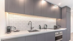Une cuisine moderne avec des meubles gris, un plan de travail blanc, un évier à deux bacs et un four encastré.