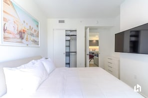 Un dormitorio con cama, armario, televisor y un cuadro en la pared.