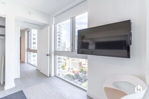 A modern apartment with a large window, a flat-screen TV mounted on the wall, and a minimalist white chair.