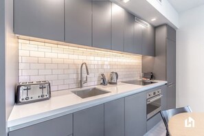 A modern kitchen with grey cabinets, a white countertop, a built-in oven, and a toaster.